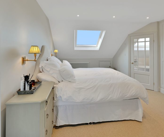 L-shaped mansard loft conversion in Chingford featuring neutral toned bedroom with skylight and en suite bathroom