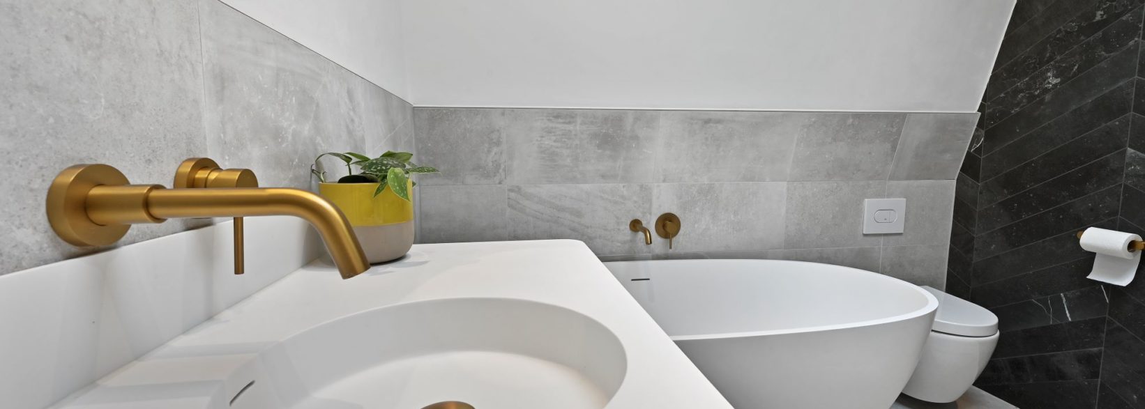 Bathroom with natural tiling and gold brassware. Mansard conversion in Abbeywood South East London
