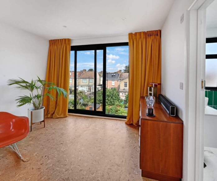 Living room with grey aluminium sliding doors leading to frameless glass balcony. A loft conversion in Hackney E9