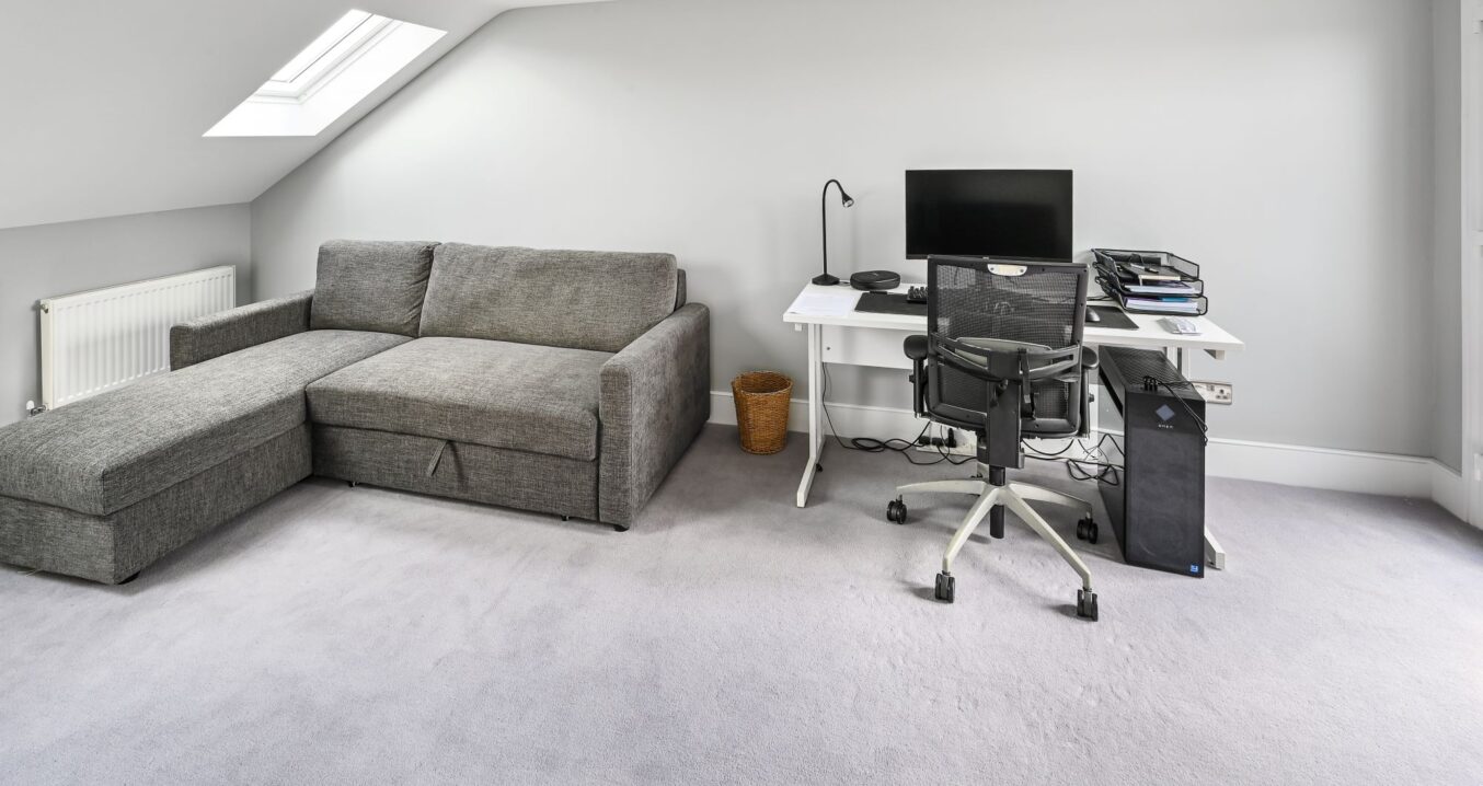Modern loft conversion annexe in Barnet North London featuring grey sofa bed, white office desk, and sloped ceiling with skylight