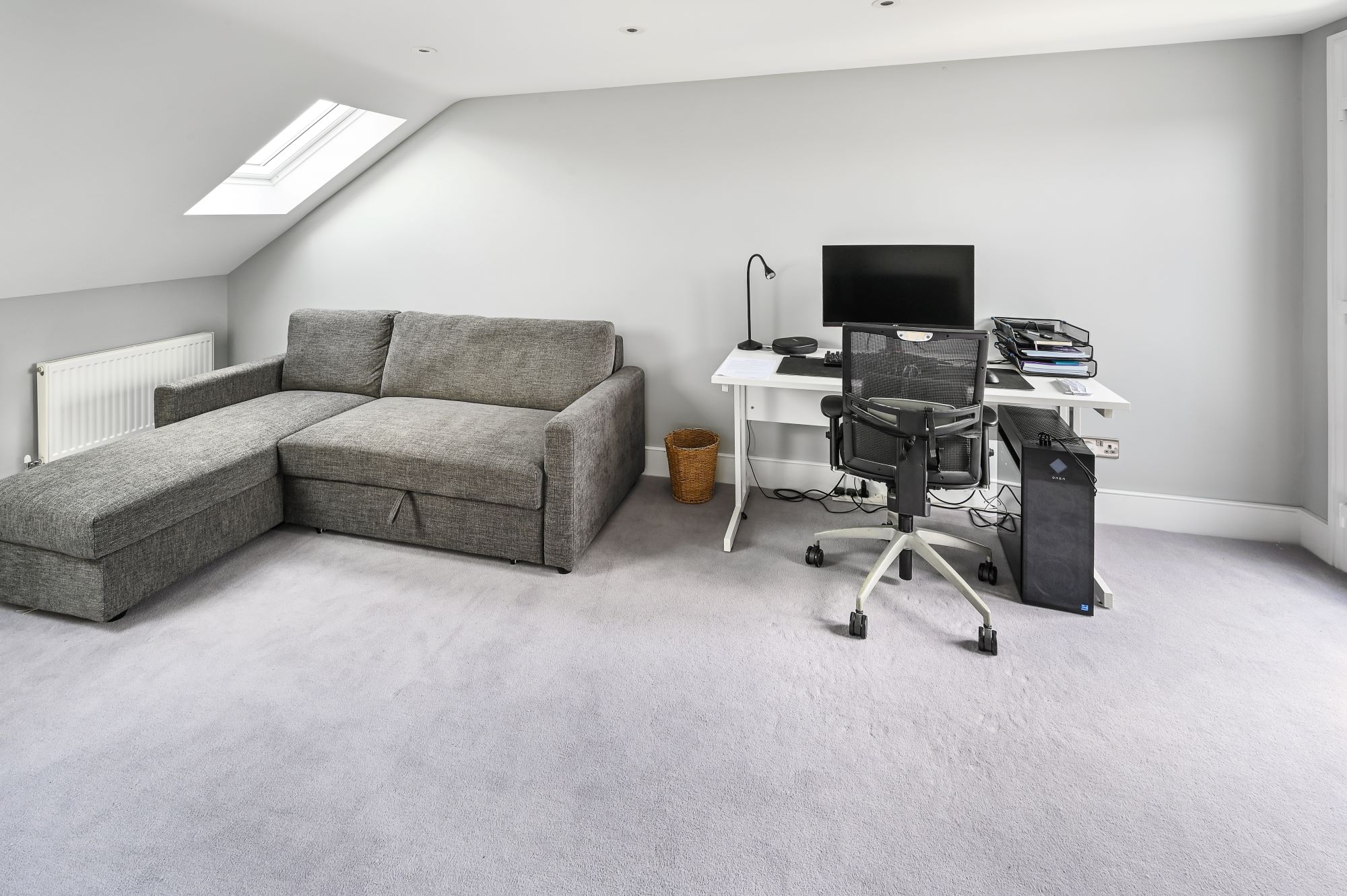 Modern loft conversion annexe in Barnet North London featuring grey sofa bed, white office desk, and sloped ceiling with skylight