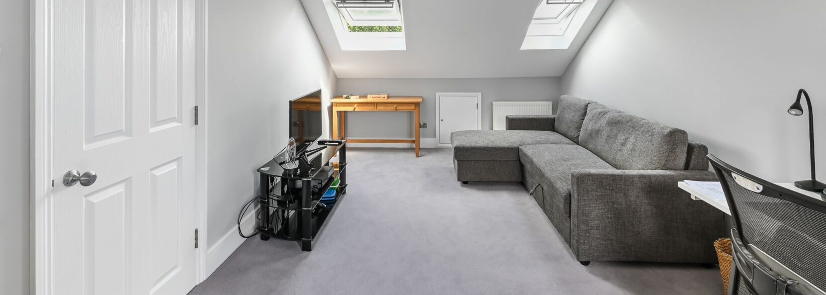Spacious loft conversion in Barnet North London with twin Velux skylights, built-in wardrobes, grey corner sofa, and open plan layout