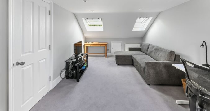 Spacious loft conversion in Barnet North London with twin Velux skylights, built-in wardrobes, grey corner sofa, and open plan layout