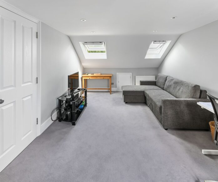 Spacious loft conversion in Barnet North London with twin Velux skylights, built-in wardrobes, grey corner sofa, and open plan layout