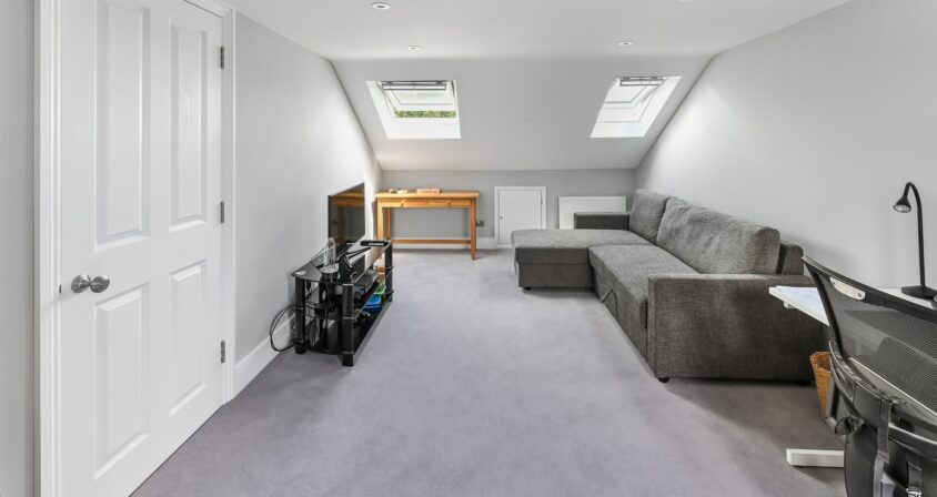 Spacious loft conversion in Barnet North London with twin Velux skylights, built-in wardrobes, grey corner sofa, and open plan layout