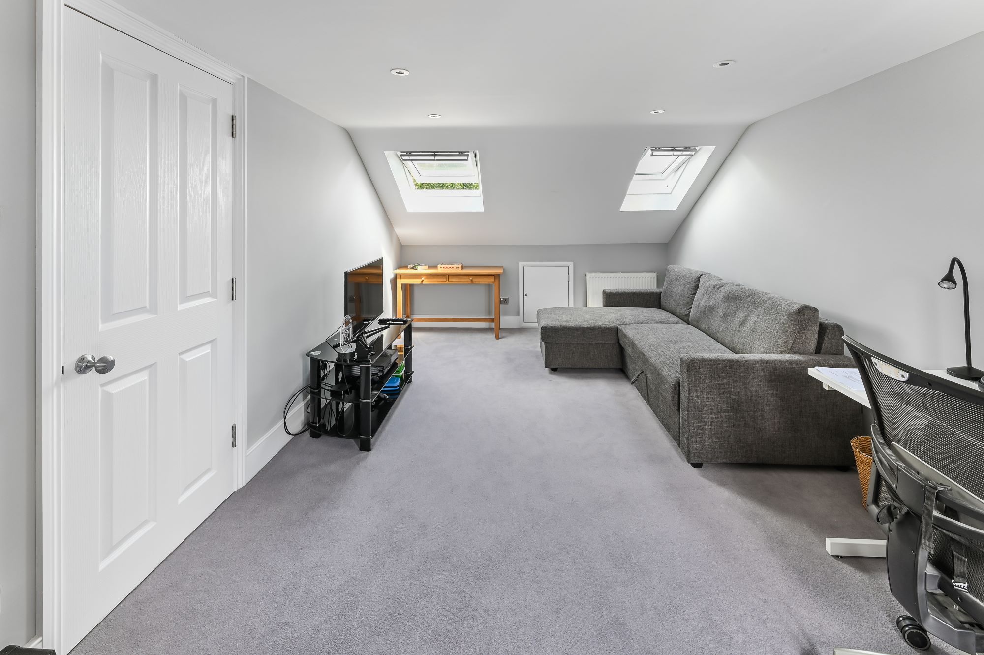 Spacious loft conversion in Barnet North London with twin Velux skylights, built-in wardrobes, grey corner sofa, and open plan layout