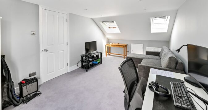 Loft conversion home office in Barnet North London with dual computer workstations, entertainment area, Velux skylights, and grey carpeting