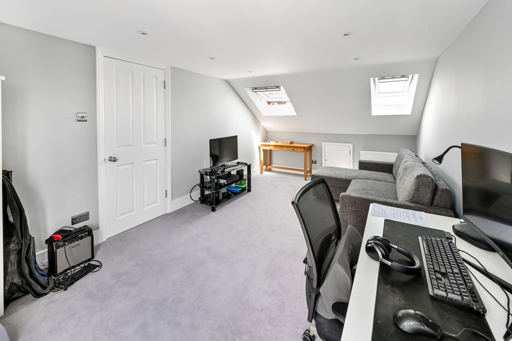 Loft conversion home office in Barnet North London with dual computer workstations, entertainment area, Velux skylights, and grey carpeting
