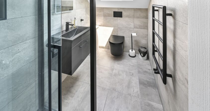 Modern ensuite bathroom in Barnet North London loft conversion with large format tiles, floating vanity, wall-hung toilet, skylight, and black fixtures