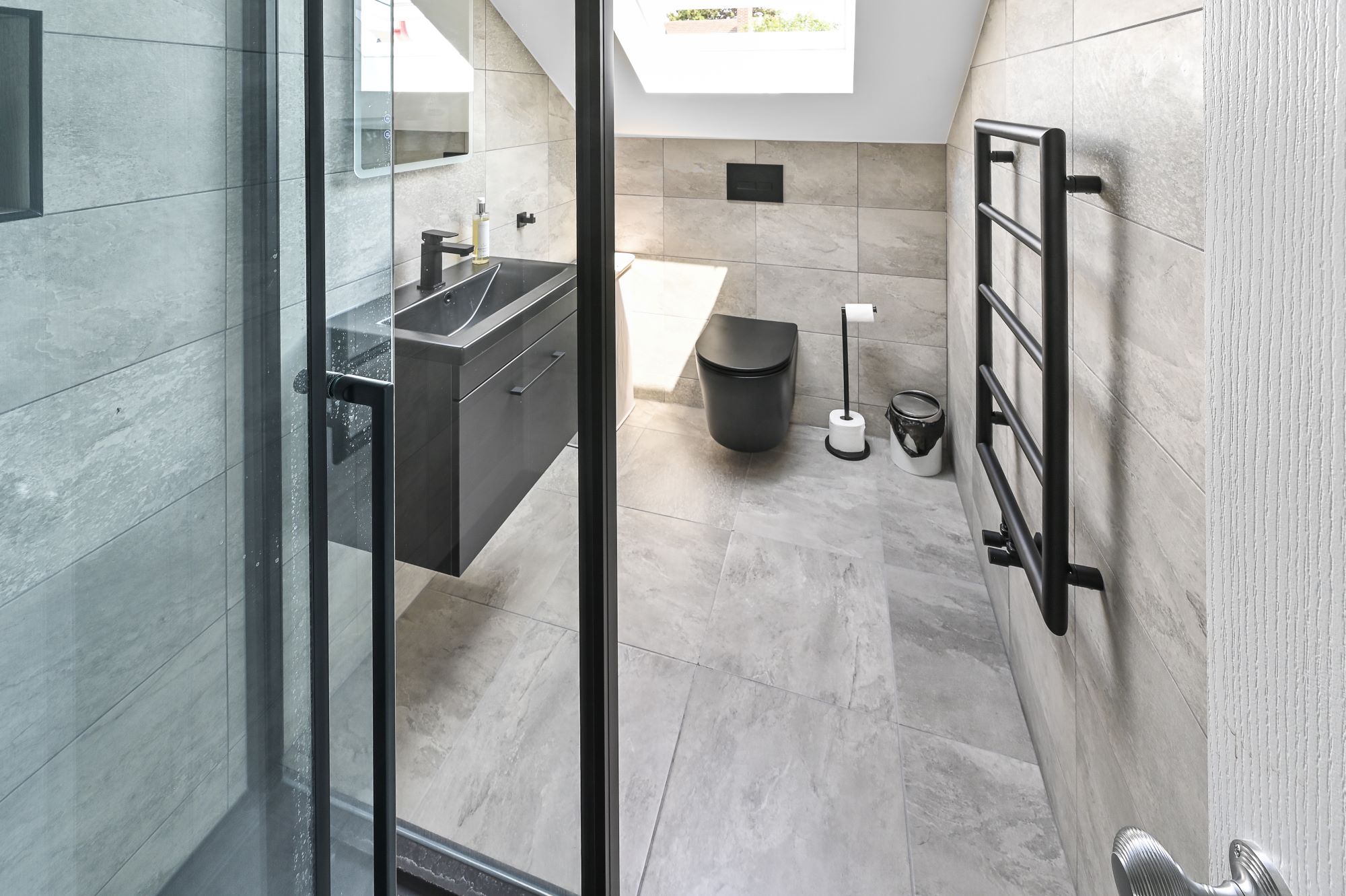 Modern ensuite bathroom in Barnet North London loft conversion with large format tiles, floating vanity, wall-hung toilet, skylight, and black fixtures
