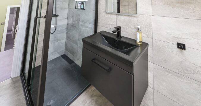 Premium bathroom vanity in Barnet loft conversion with black floating unit, integrated basin, glass shower enclosure, and stone tiles