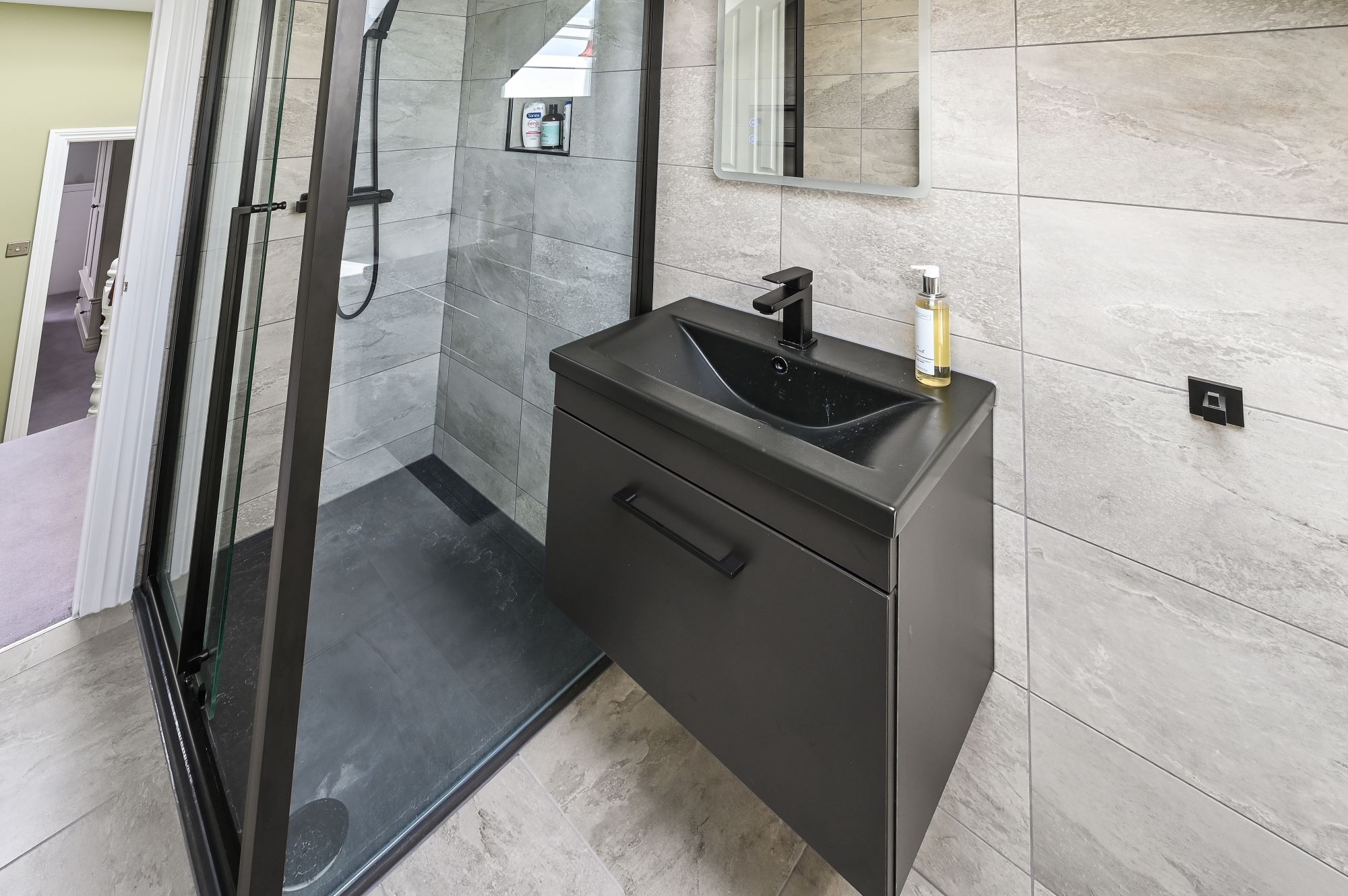 Premium bathroom vanity in Barnet loft conversion with black floating unit, integrated basin, glass shower enclosure, and stone tiles