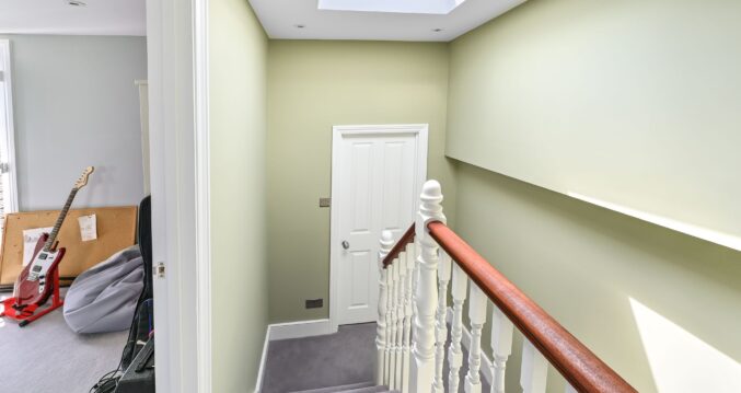 L-shaped dormer loft conversion staircase in Barnet North London with traditional white spindles, mahogany handrail, skylight, and sage green walls