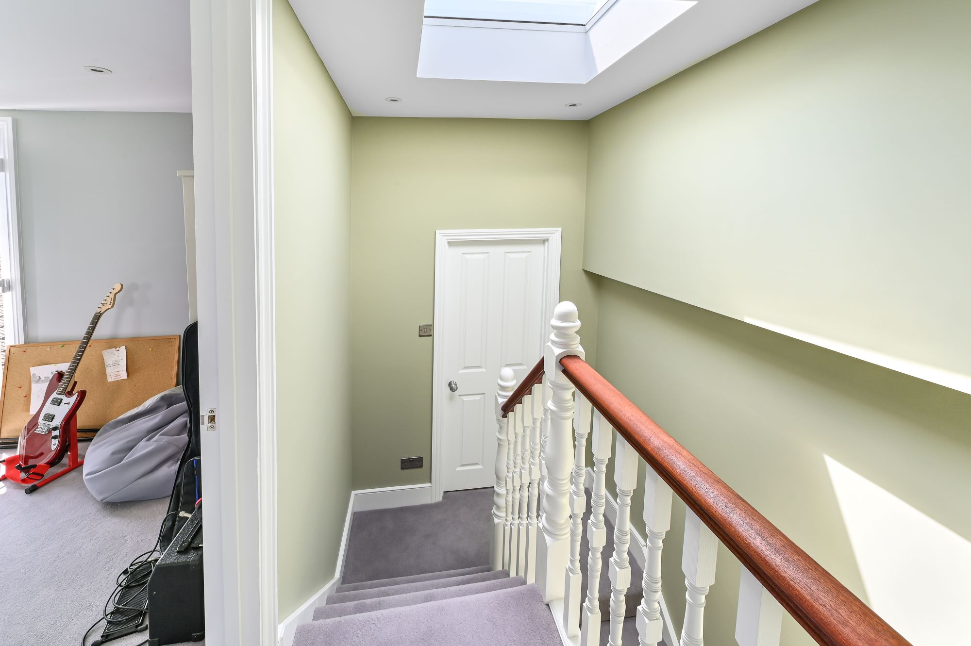L-shaped dormer loft conversion staircase in Barnet North London with traditional white spindles, mahogany handrail, skylight, and sage green walls