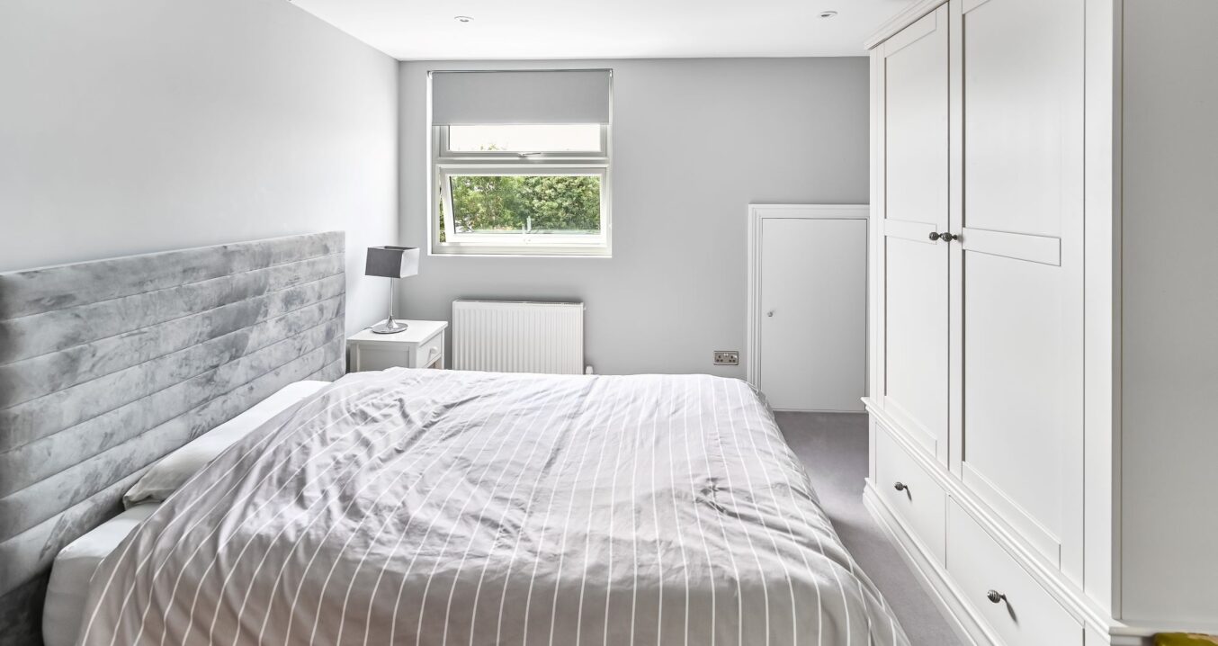 Loft conversion bedroom in Barnet North London with built-in white wardrobes, dormer window, grey upholstered bed, and fitted storage