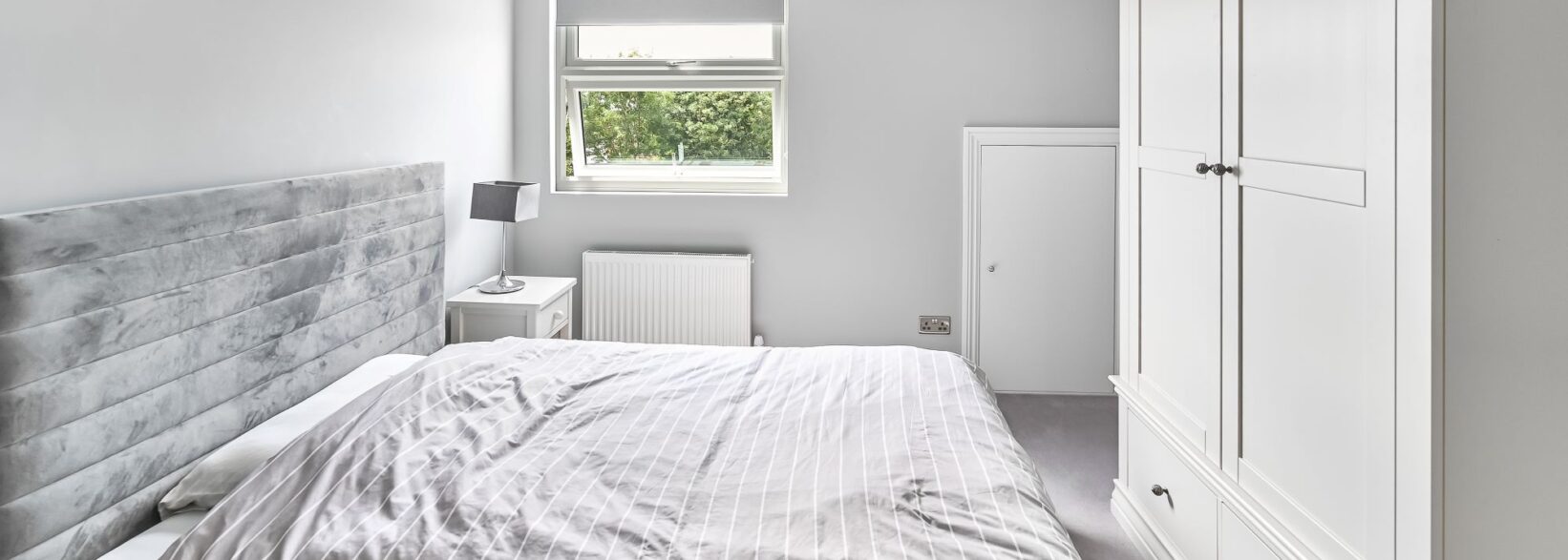 Loft conversion bedroom in Barnet North London with built-in white wardrobes, dormer window, grey upholstered bed, and fitted storage