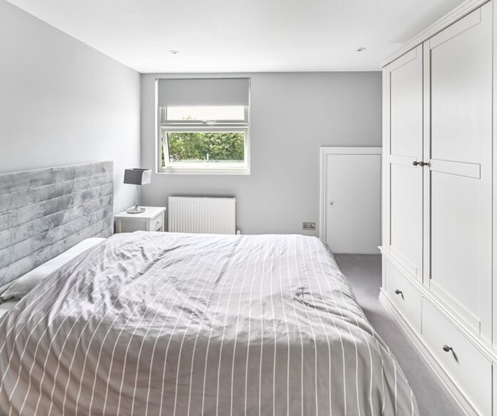 Loft conversion bedroom in Barnet North London with built-in white wardrobes, dormer window, grey upholstered bed, and fitted storage