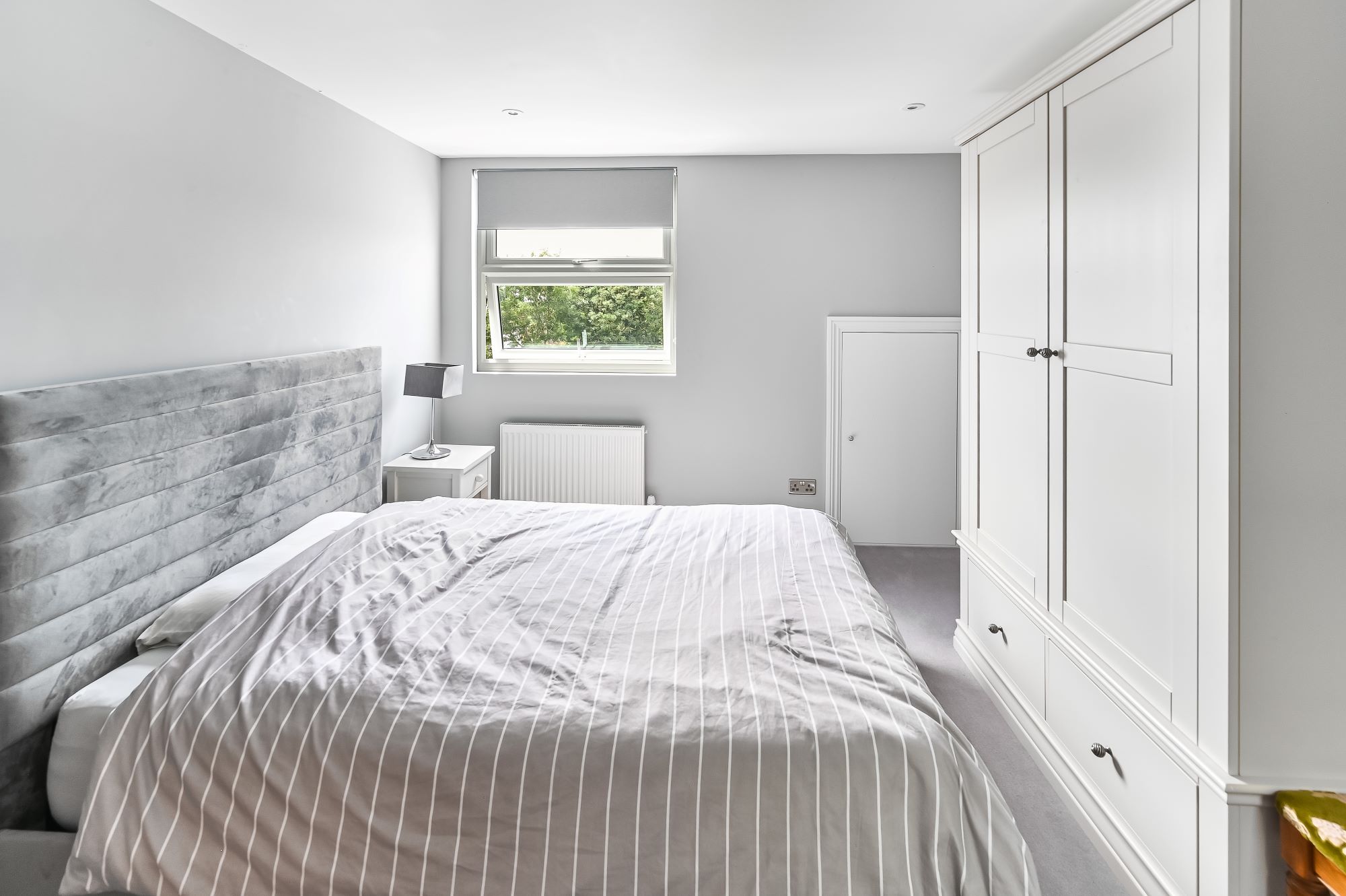 Loft conversion bedroom in Barnet North London with built-in white wardrobes, dormer window, grey upholstered bed, and fitted storage