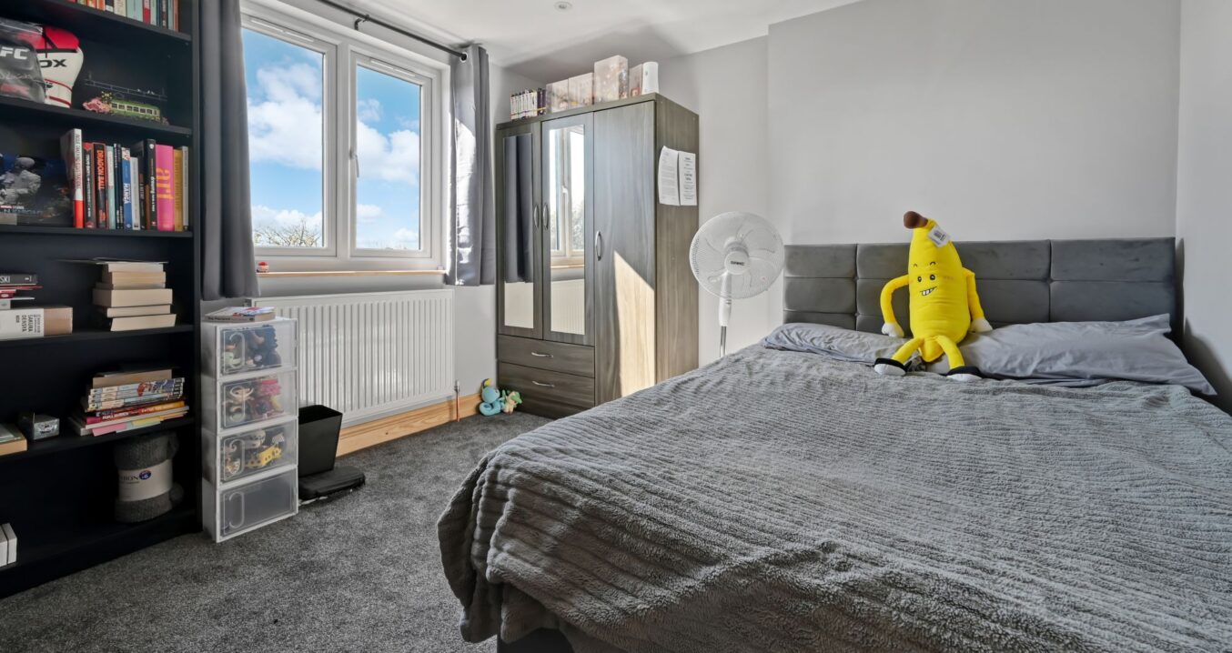 Contemporary double bedroom in Woolwich SE18 loft conversion with grey upholstered headboard, large windows, and stylish furnishings