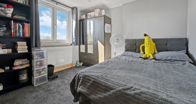 Contemporary double bedroom in Woolwich SE18 loft conversion with grey upholstered headboard, large windows, and stylish furnishings