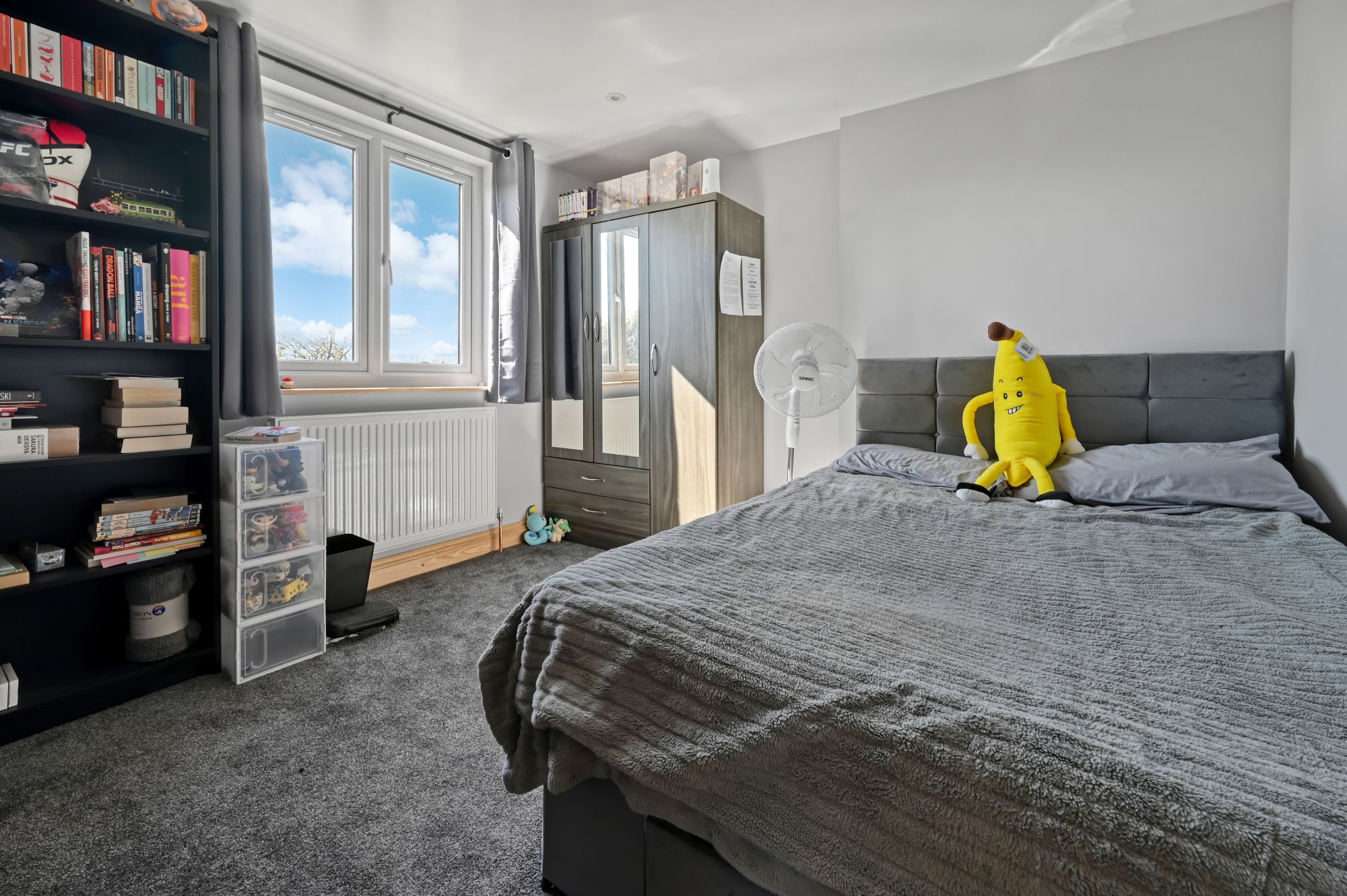 Contemporary double bedroom in Woolwich SE18 loft conversion with grey upholstered headboard, large windows, and stylish furnishings