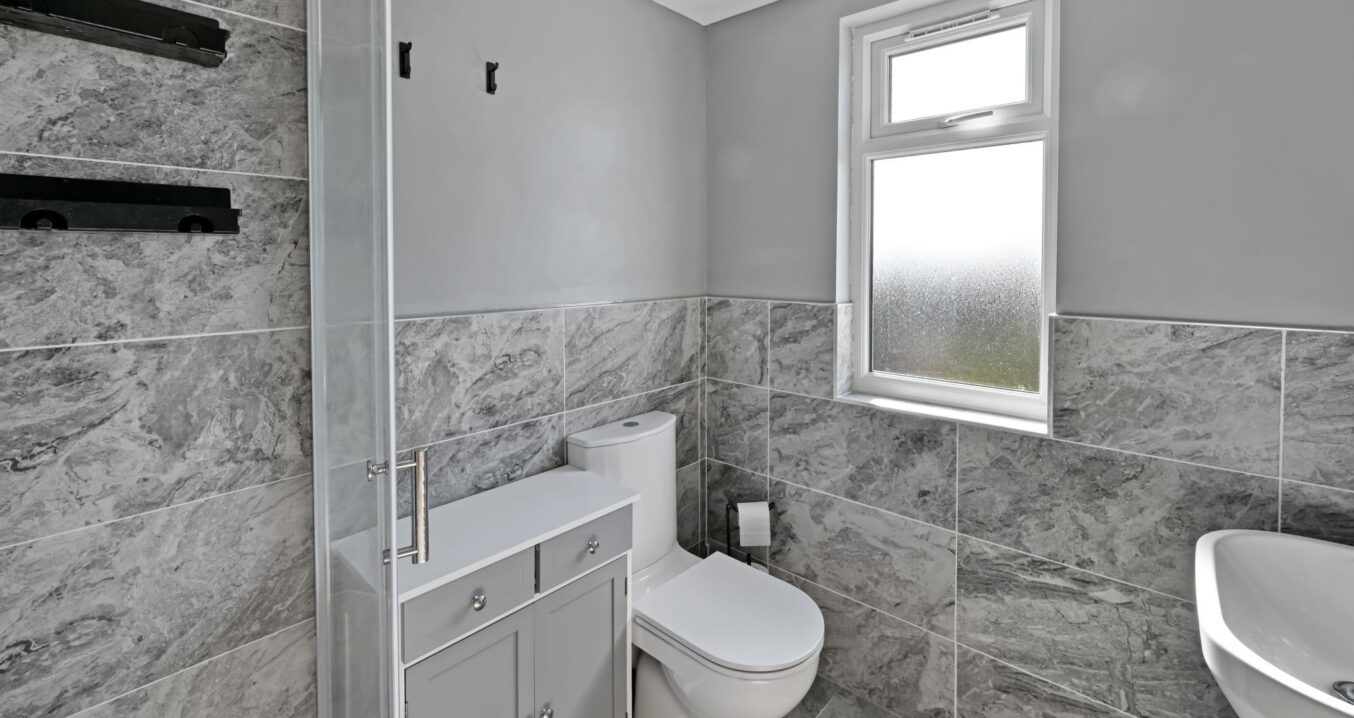 Close-up view of a modern bathroom with grey marble tiles, white toilet, and built-in grey storage unit in the Woolwich SE18 loft conversion