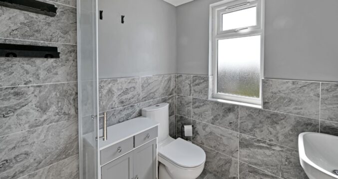Close-up view of a modern bathroom with grey marble tiles, white toilet, and built-in grey storage unit in the Woolwich SE18 loft conversion