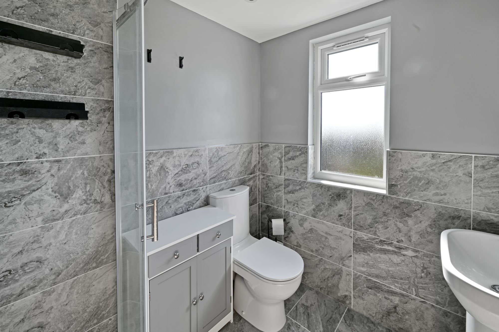 Close-up view of a modern bathroom with grey marble tiles, white toilet, and built-in grey storage unit in the Woolwich SE18 loft conversion