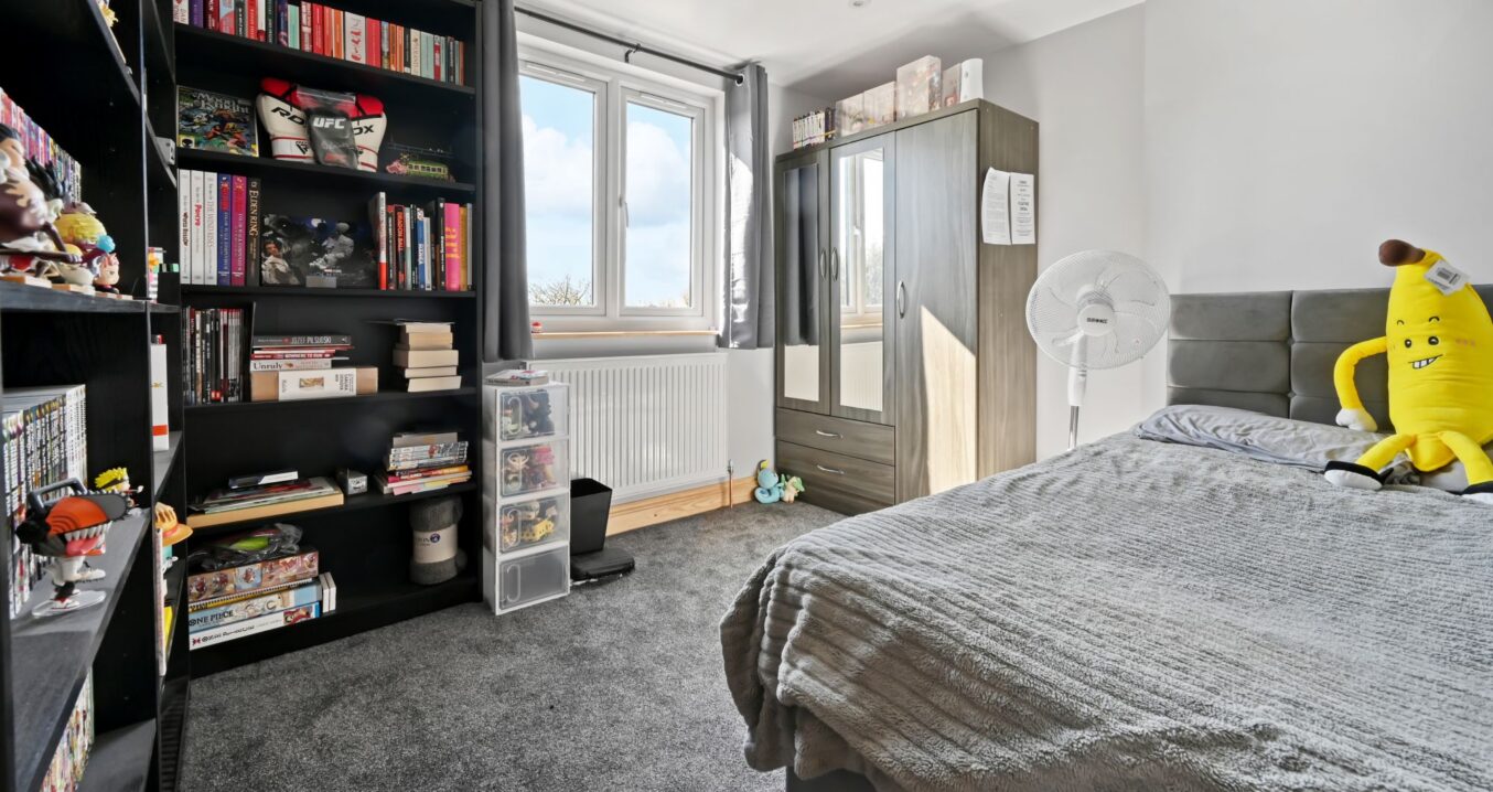 Modern loft bedroom showcasing a tall black bookshelf filled with books and collectibles, double bed, and natural light in Woolwich SE18
