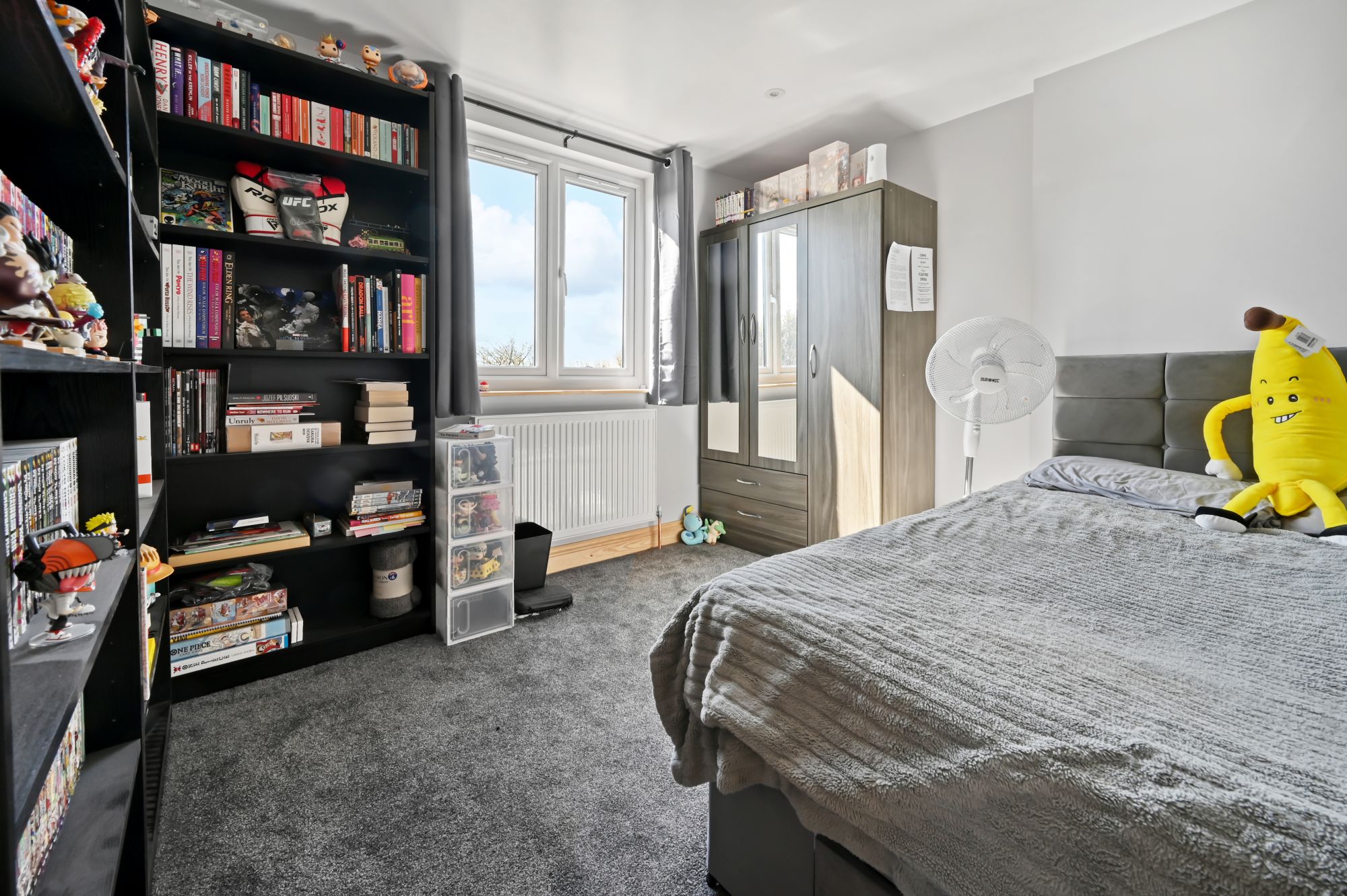 Modern loft bedroom showcasing a tall black bookshelf filled with books and collectibles, double bed, and natural light in Woolwich SE18