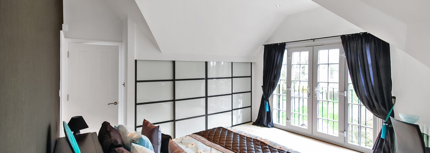 Contemporary hip to gable loft conversion bedroom in Barnet featuring black framed sliding wardrobes and bifold doors