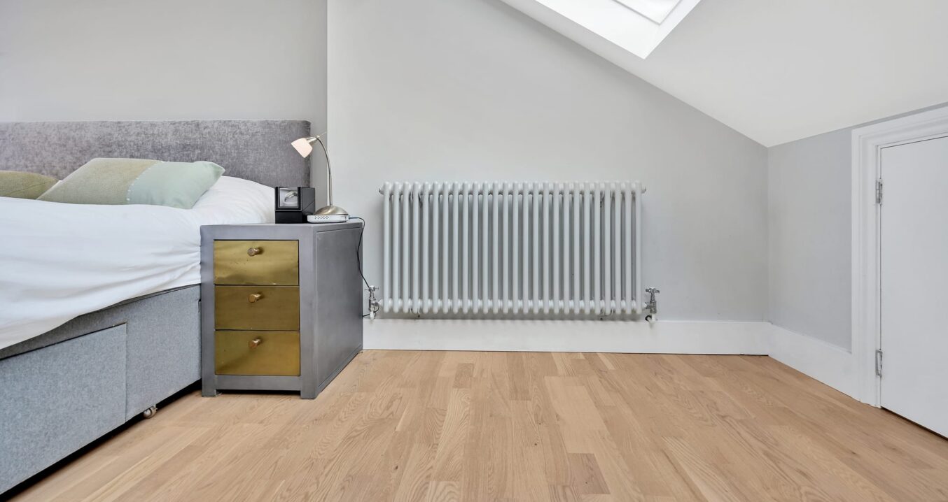 Modern loft conversion bedroom in Edgware showing light wood flooring, grey upholstered bed and large rooflight