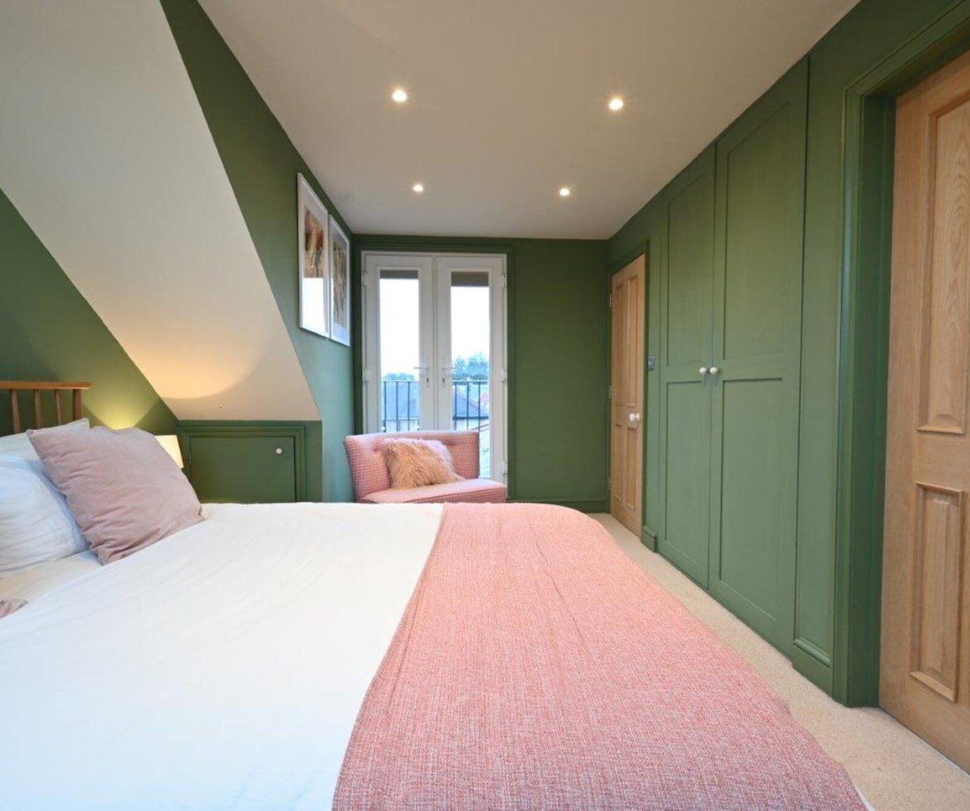 Stylish green painted bedroom with wooden bed frame and pink bedding in a Walthamstow E17 loft conversion