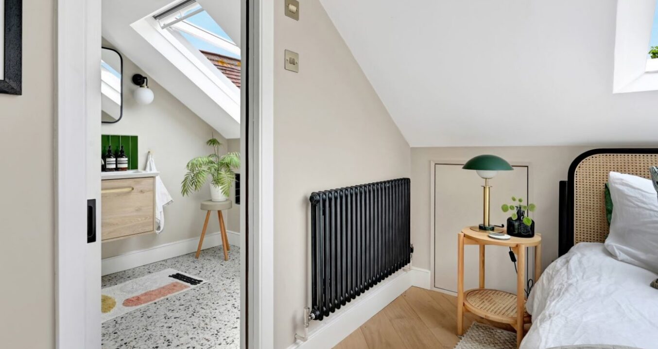 Loft bedroom in Harrow with en suite doorway, radiator, sloping ceiling and natural timber flooring