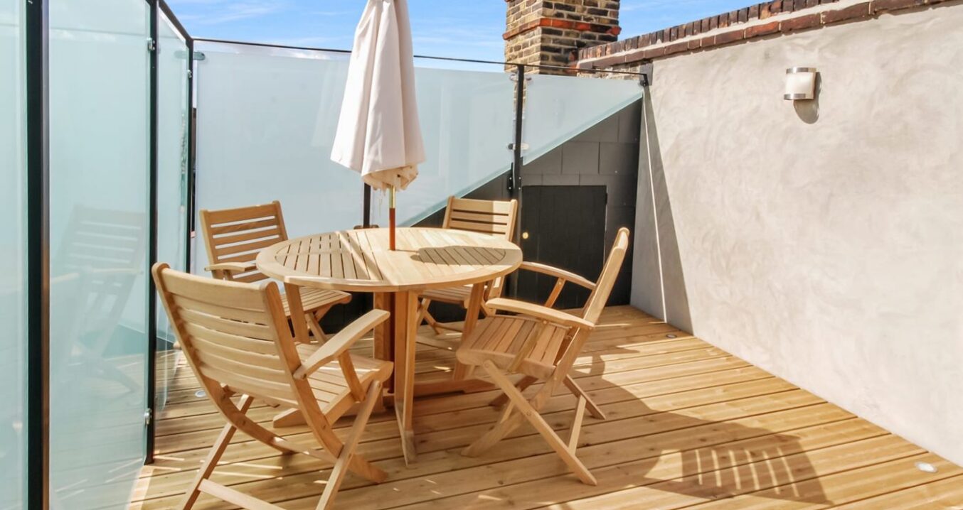 Roof terrace in a Borehamwood loft conversion with timber decking, glass balustrade and outdoor seating area