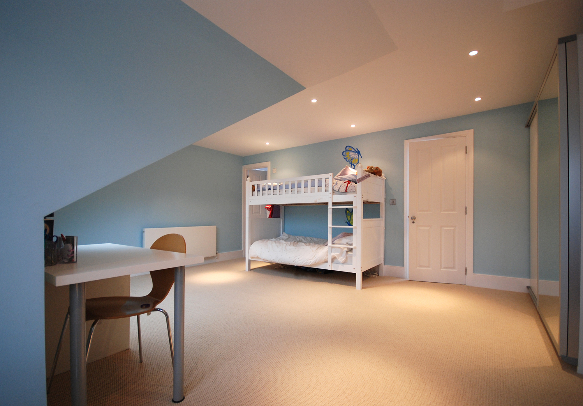 Fun loft conversion children’s bedroom in Edgware with white bunk beds, blue walls and clever use of sloping ceilings