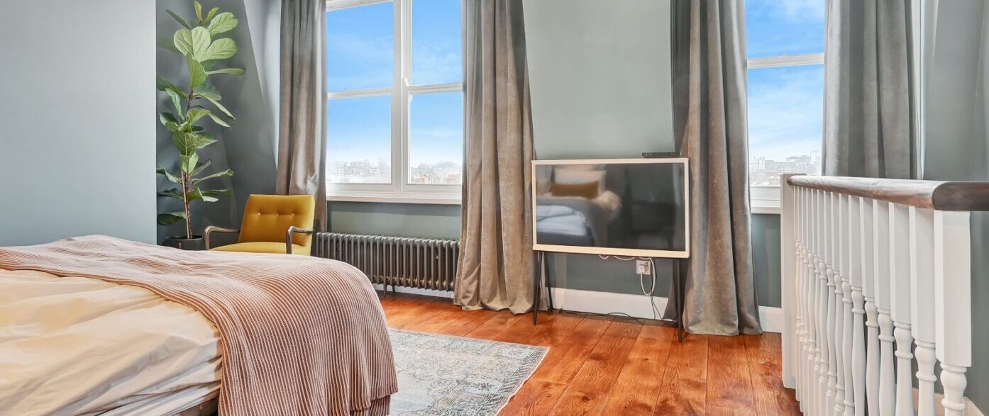 High-end mansard loft conversion bedroom in Barnet with large windows and impressive city views. Premium finish.