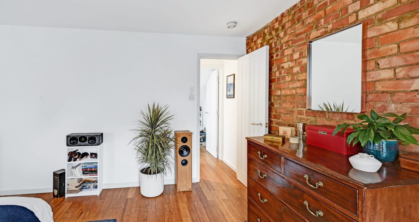 Loft bedroom with exposed brick feature wall, timber floor and white walls for a Plumstead SE18 style home