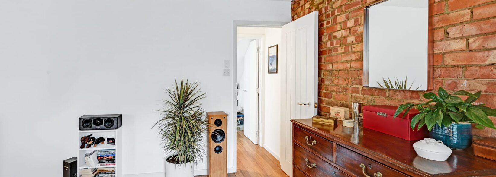 Loft bedroom with exposed brick feature wall, timber floor and white walls for a Plumstead SE18 style home