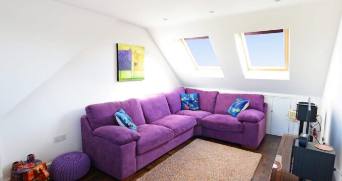 Spacious purple velvet L-shaped sofa in a bright loft living area with roof windows in Walthamstow E17