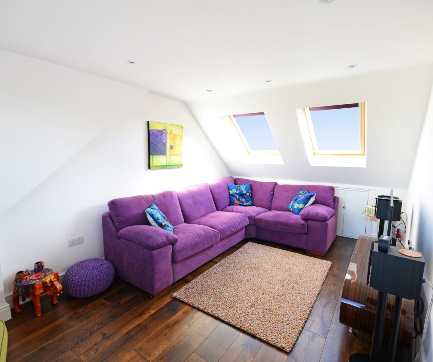 Spacious purple velvet L-shaped sofa in a bright loft living area with roof windows in Walthamstow E17