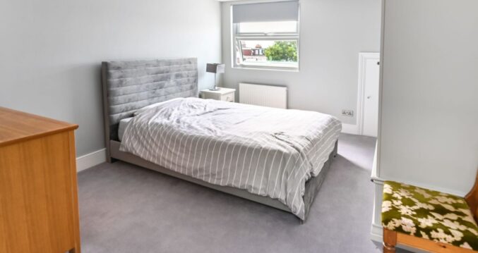 Modern dormer loft conversion master bedroom in Barnet with grey velvet headboard and large window