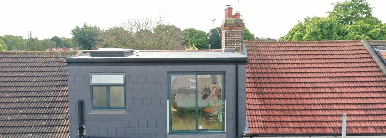 Rear exterior of a Stanmore HA7 loft conversion with a dark dormer, flat roof and large glazing