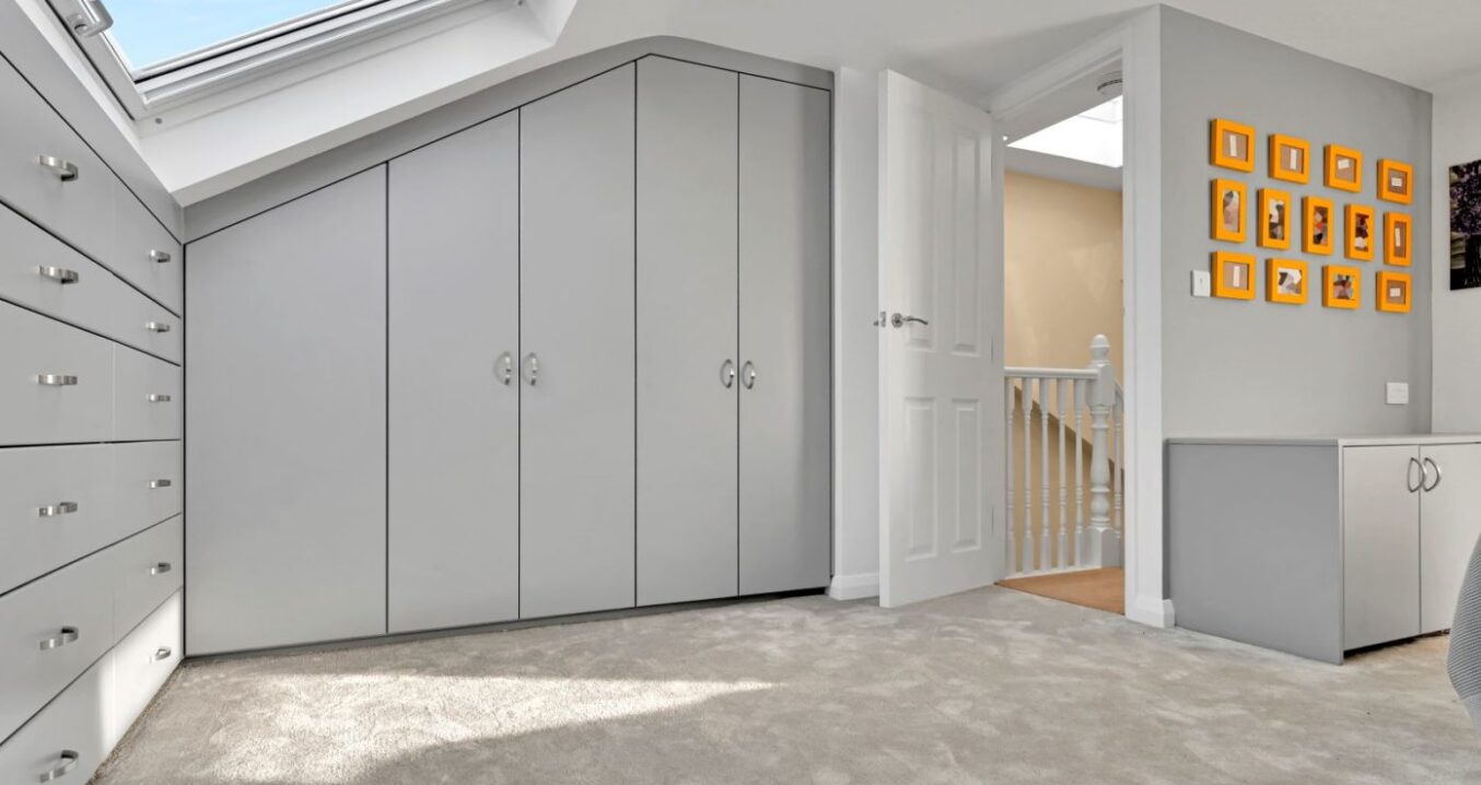 Light grey fitted wardrobes beneath a sloping loft ceiling with a rooflight above.