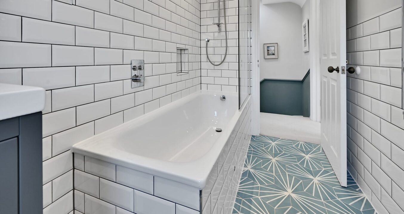 Loft conversion bathroom with white tiling, bath, shower screen and blue patterned floor for an Epping CM16 property.