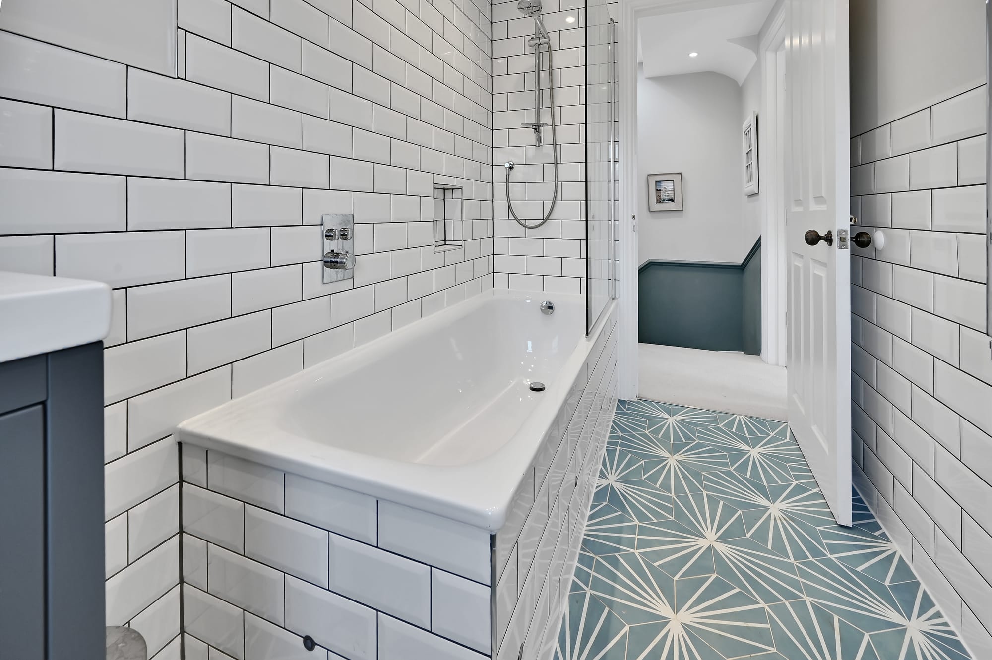 Loft conversion bathroom with white tiling, bath, shower screen and blue patterned floor for an Epping CM16 property.