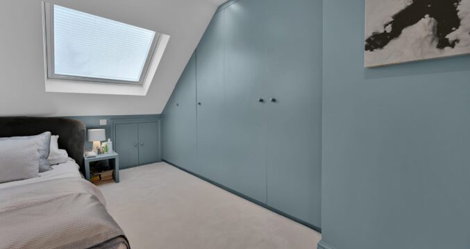 Loft conversion bedroom with fitted wardrobes, roof window and teal storage wall for an Epping CM16 home.