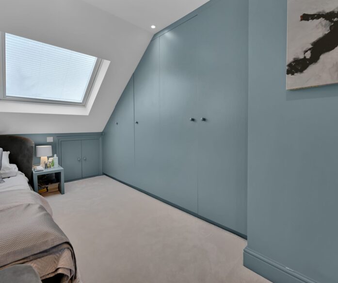 Loft conversion bedroom with fitted wardrobes, roof window and teal storage wall for an Epping CM16 home.
