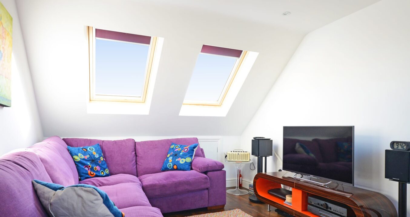 Loft conversion living room with roof windows, purple sofa and sloping ceiling for an Epping CM16 property.