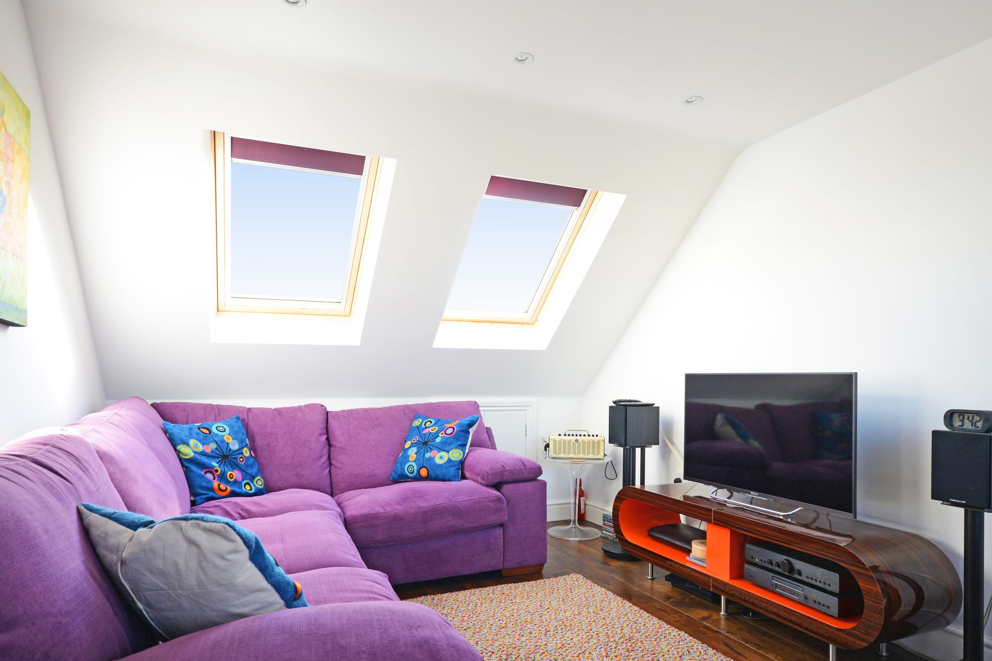 Loft conversion living room with roof windows, purple sofa and sloping ceiling for an Epping CM16 property.